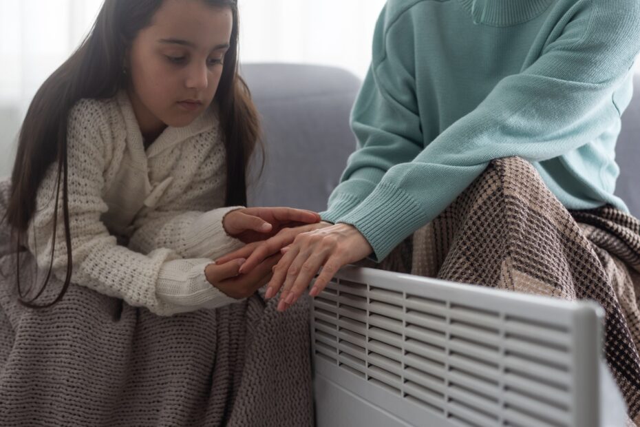 Mutter und Tochter in Decken eingehüllt vor Heizung