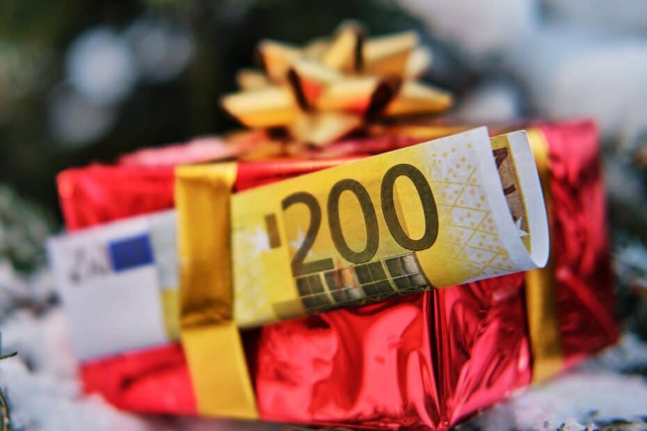 Verpacktes Geschenk mit eingesteckten 200 Euro Schein vor Weihnachtsbaum