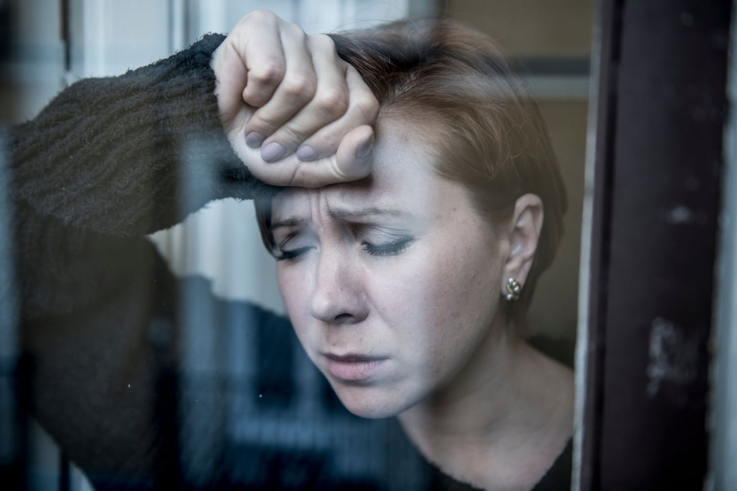 Verzweifelte Frau lehnt am Fenster