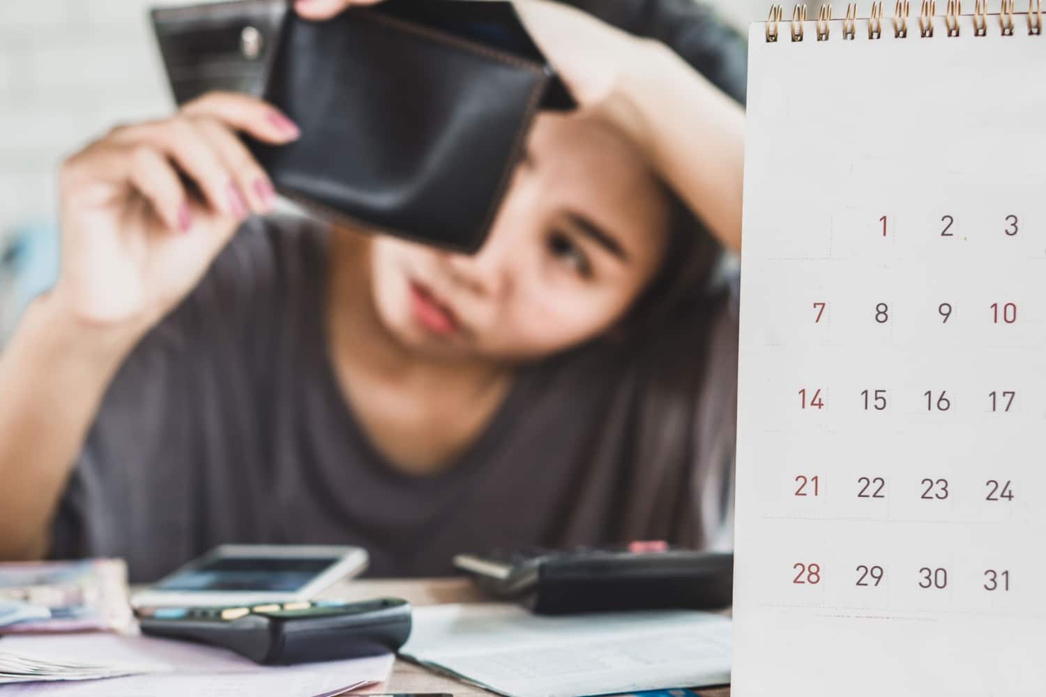 Eine Person mit besorgtem Gesichtsausdruck hält eine leere Geldbörse in der Hand. Im Vordergrund ist ein Kalender zu sehen, der ein Gefühl von zeitlichem Druck vermittelt.